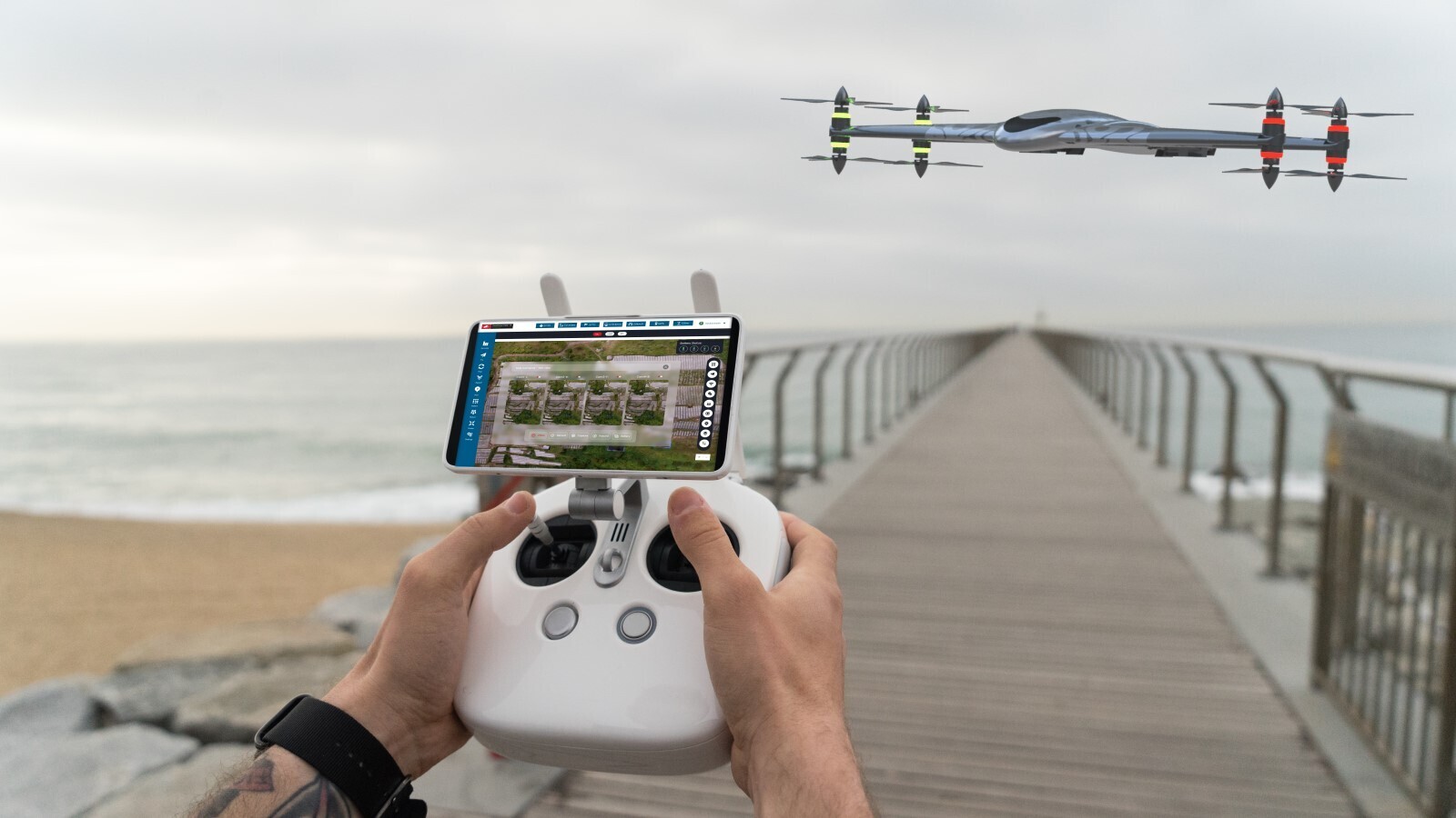 Person controlling a drone with a remote as it flies over a pier near the ocean